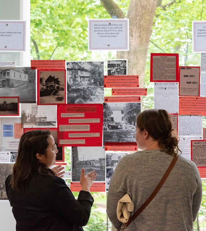 Students talk in front of window-mounted public history poster project on Reno City