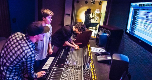 Three students adjust knobs on a soundboard.