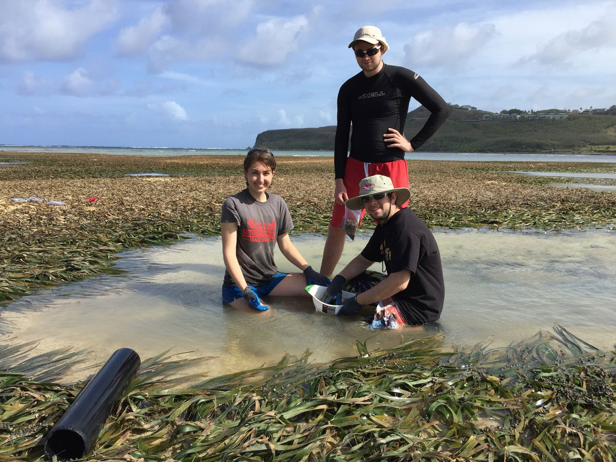 Students and professor, wearing gloves and holding a bucket, work outside in a lake