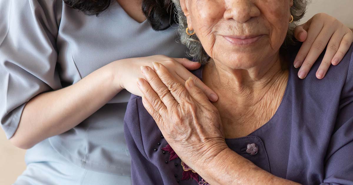 Young woman in scrubs puts hands on the shoulders of elderly woman