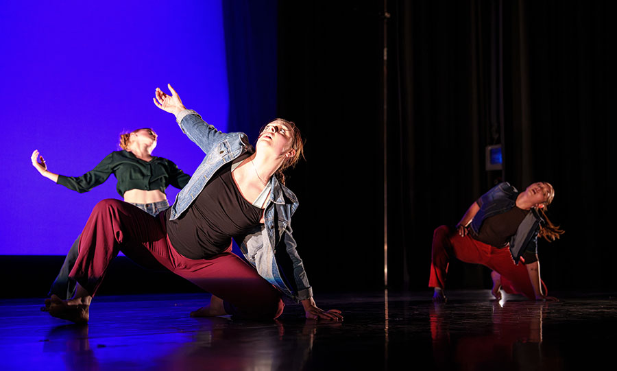 Three dancers doing floorwork with dramatic underlighting