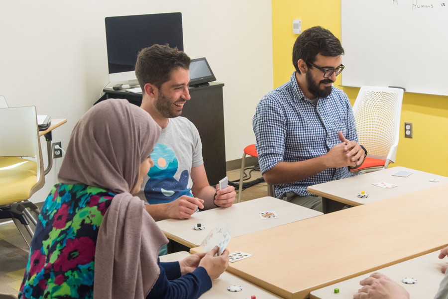 Three people play a game involving playing cards and chips