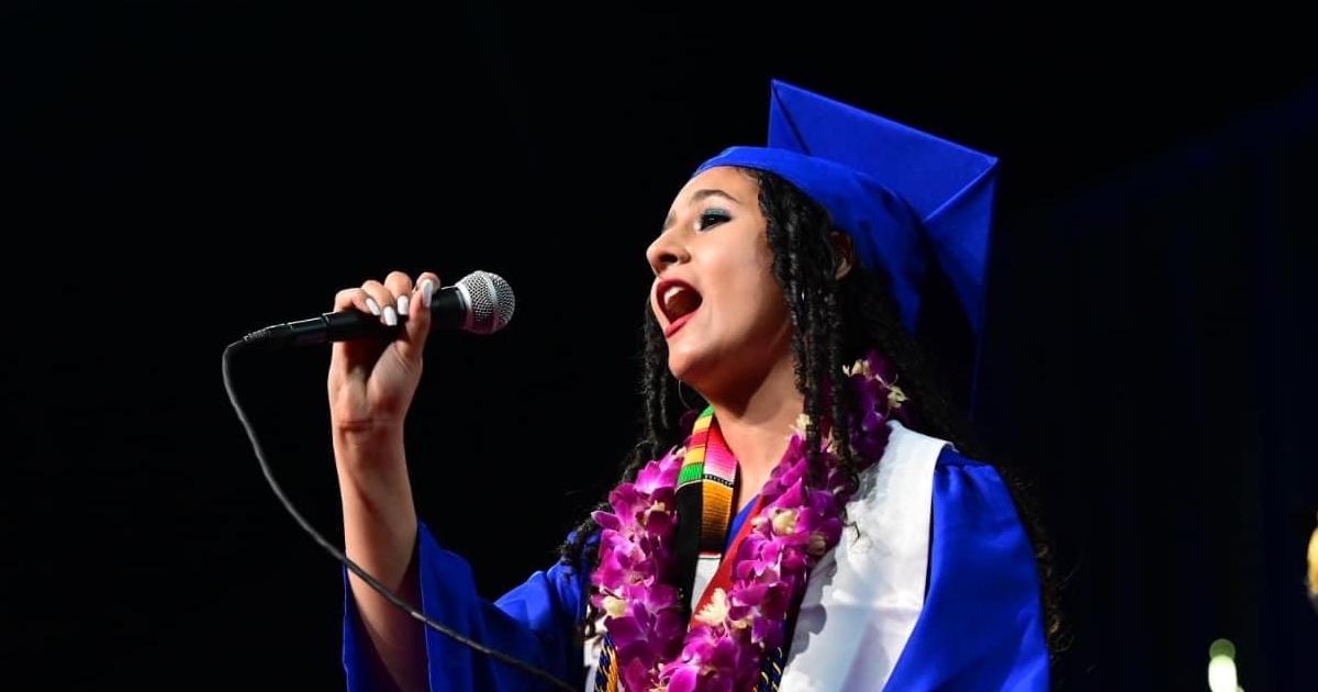 Aisley Wallace Harper, dressed in graduation regalia, sings the national anthem at the CAS May 2023 graduation ceremony