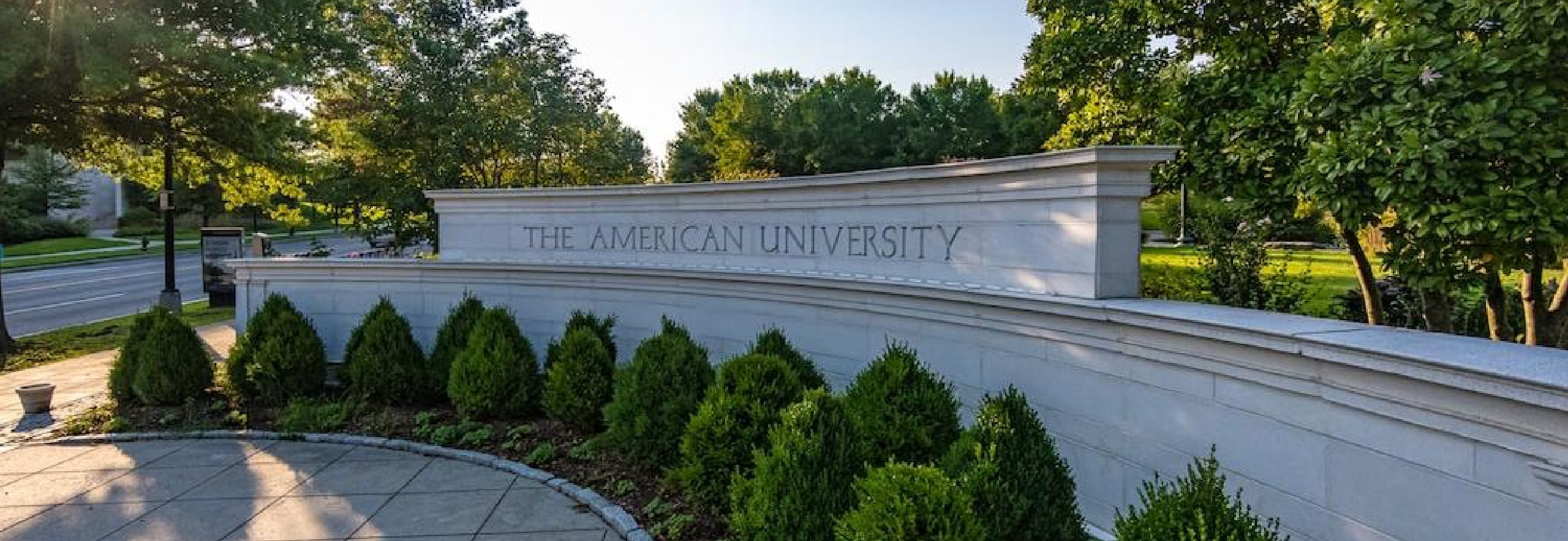 American University entrance with bushes and tress around brick structure with the name of the university