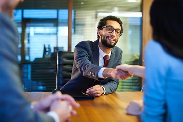 Man and woman seated at table shaking hands during meeting