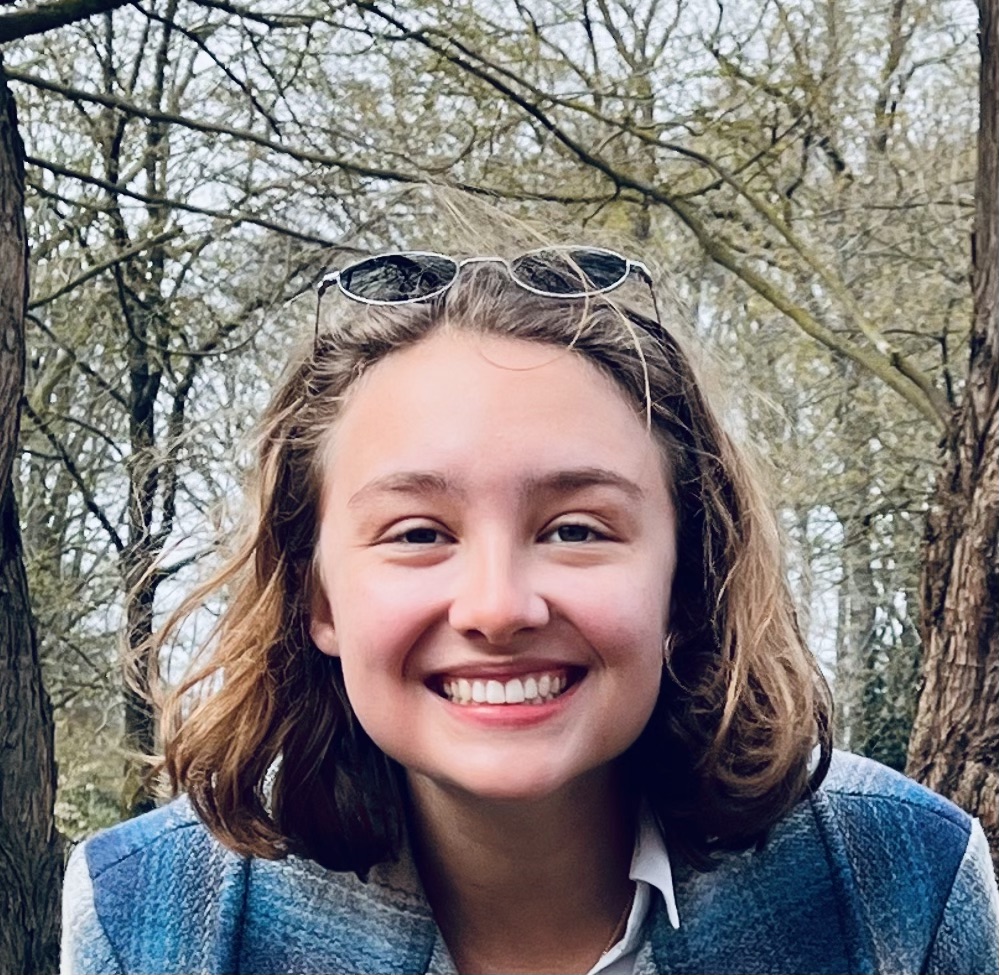 A close-up photo of Hannah with classes resting on the top of her head and a forest in the background