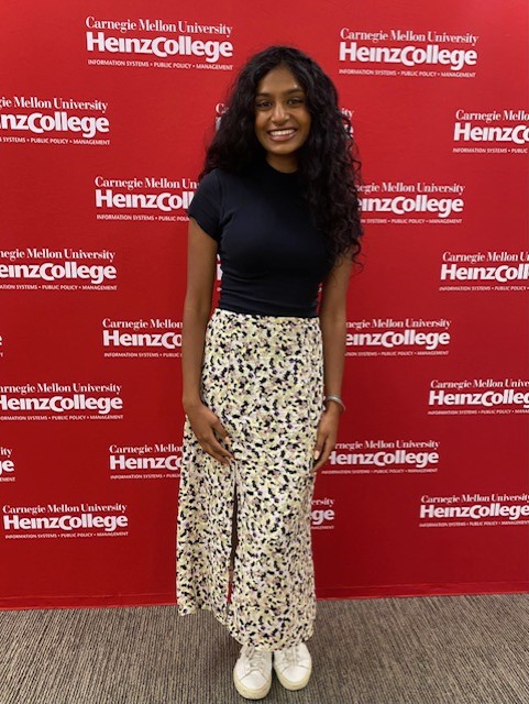 Sarina in a black shirt and white skirt standing in front of a red background