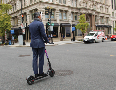 man in a suit rides a scooter through the streets of DC