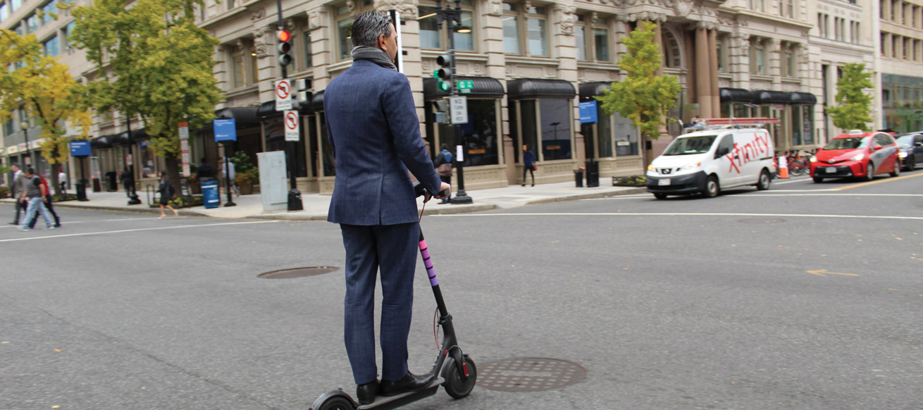 man in a suit rides a scooter through the streets of DC