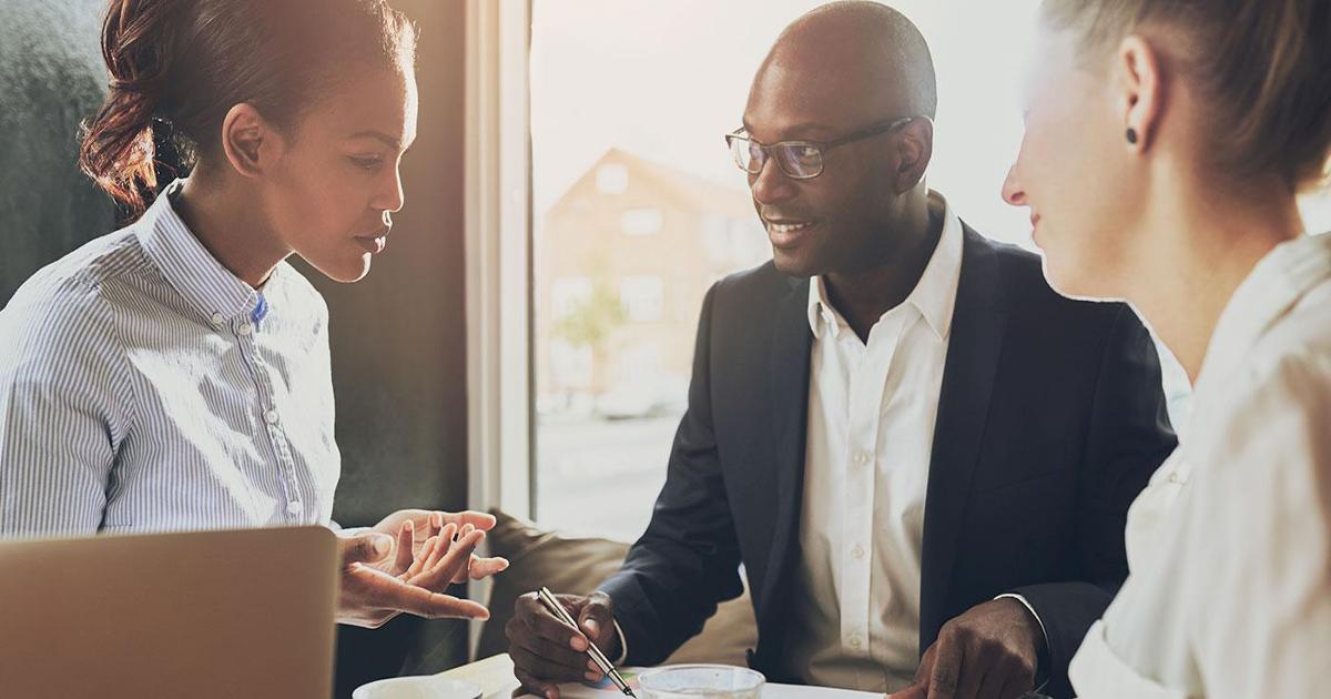 Two women and a man sitting in a small table talking in business atire.