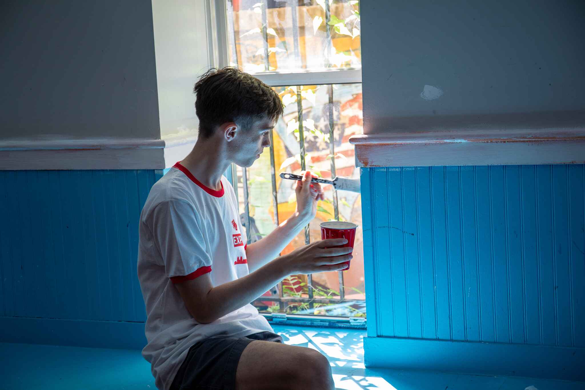 Student sitting in window sill painting wall.