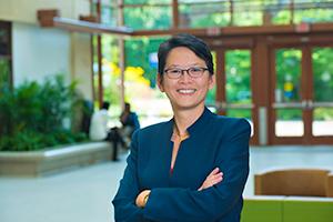 SIS dean standing in the atrium with doorway and plants in the background.